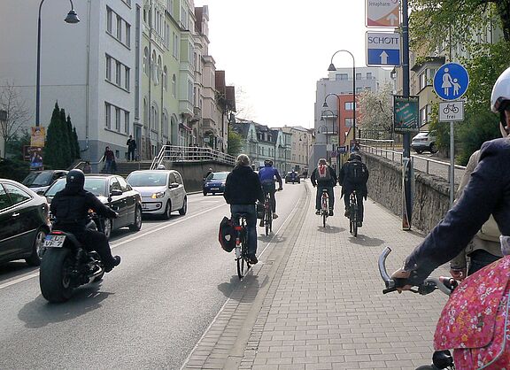 Radfahrer fahren auf der Straße sowie auf Fußweg eine Steigung hinauf