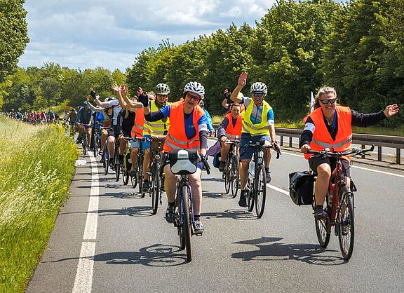 viele Radfahrende fahren auf einer Baumbesäumten Straße