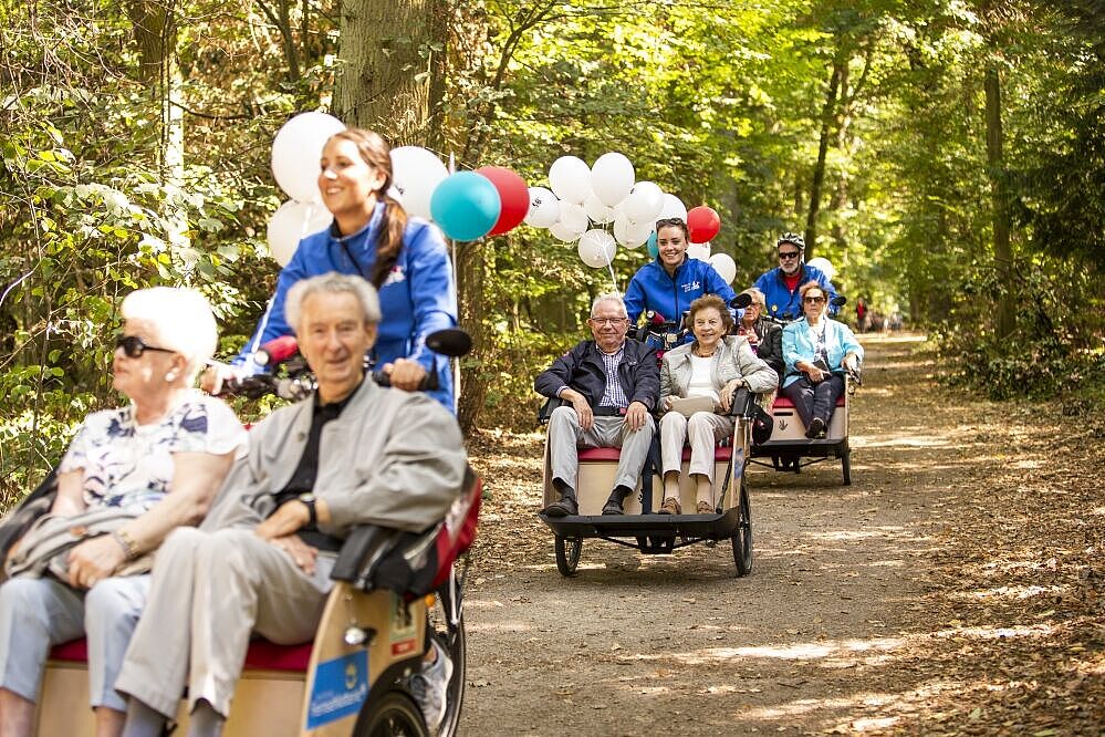 Mehrere Rikschas mit Senioren fahren über einen Waldweg