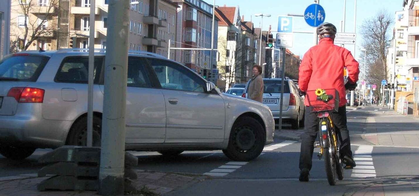 Radfahrer hält vor einem Auto, das seine Spur kreuzt Radfahrer hält vor einem Auto, das seine Spur kreuzt