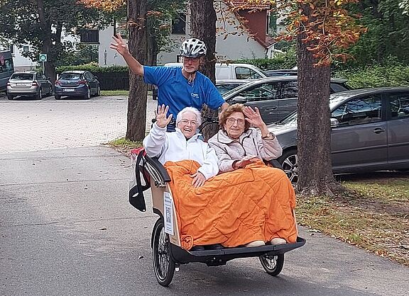 Zwei Frauen werden in einer Fahrrad-Rikscha gefahren und winken